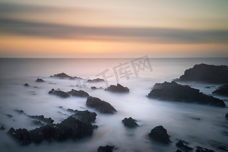 令人惊叹的长时间曝光的岩石上的海洋在充满活力的日落时的风景图像