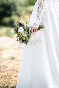 花边摄影照片_新娘的花束从锥和棉花关闭了在新娘的手中花边礼服森林背景