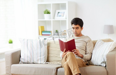休闲，文学和人概念-人坐在沙发和读书在家。一个男人坐在沙发上看书在家里