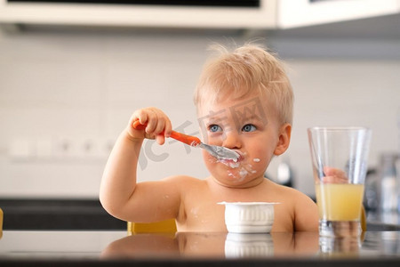可爱的一岁男婴用勺子吃酸奶。蹒跚学步的孩子脏兮兮的脸。