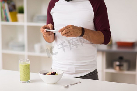 健康饮食，科技和人的概念-在家中厨房吃早餐的智能手机人。带着智能手机的男人在家吃早饭