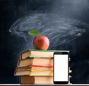 学校用品对着黑板。回学校去。智能手机、书籍和新鲜苹果与黑板