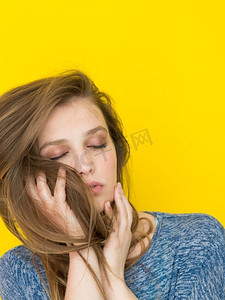 丝质摄影照片_一位美丽积极的年轻女子玩耍着黄色背景下孤立的丝质长发