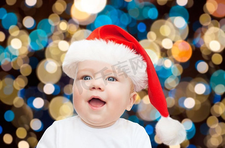 圣诞节，节日和人们的概念-戴着圣诞帽的小男孩在灯光下的背景。圣诞节戴着圣诞帽的小男婴