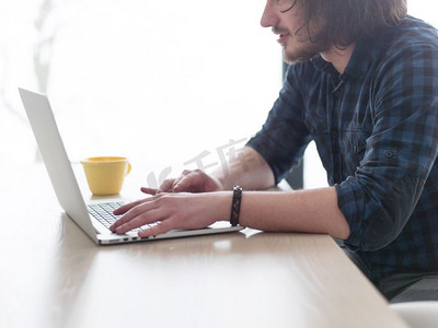 一个年轻人一边喝着咖啡，一边在家里用笔记本电脑工作