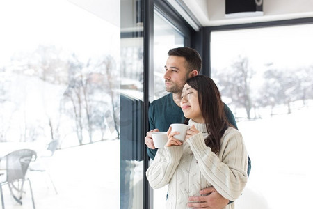 享受早晨咖啡的愉快的年轻多种族夫妇在寒冷的冬天天在家