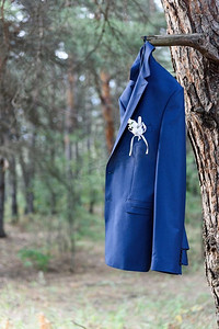 一件新郎的蓝色夹克挂在森林里的树枝上