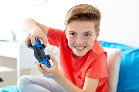 游戏，技术和人的概念-微笑的男孩，带着游戏手柄在家玩电子游戏。带着游戏手柄在家玩电子游戏的快乐男孩