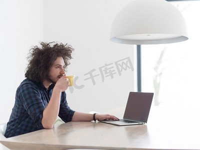 从上面摄影照片_一个年轻人一边喝着咖啡，一边在家里用笔记本电脑工作