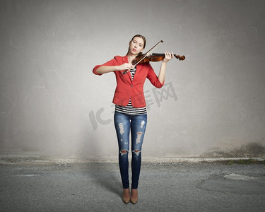 漂亮女人会拉小提琴。穿着红色夹克的年轻漂亮女子在拉小提琴