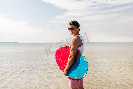 滑板、水上运动和人的概念-在夏季海滩上带着滑板微笑的年轻人。夏日海滩玩滑板的快乐小伙