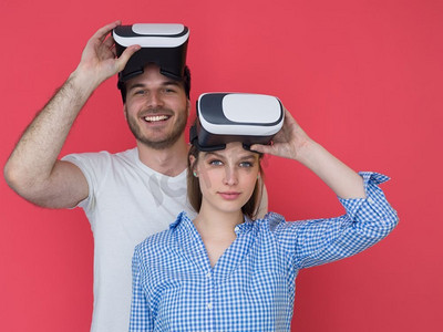 快乐的年轻夫妇在红色背景下使用虚拟现实的VR耳机眼镜获得体验