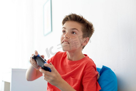 孩子电子游戏摄影照片_游戏，技术和人的概念-微笑的男孩，带着游戏手柄在家玩电子游戏。带着游戏手柄在家玩电子游戏的快乐男孩