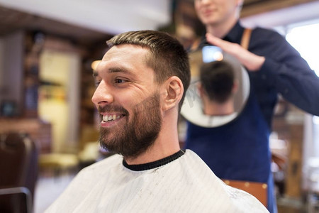 美容，发型和人的概念-理发店的男人和发型师或带镜子的理发师。理发店里带着镜子的男士和理发师
