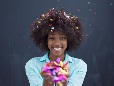舞蹈新年摄影照片_美丽的年轻黑人妇女庆祝新年和chrismas党，同时吹五彩纸屑装饰对照相机隔绝在灰色背景