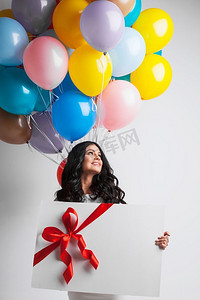 拿礼物的女人摄影照片_拿着气球和礼物的女人。带着气球和大礼盒的微笑的年轻女子