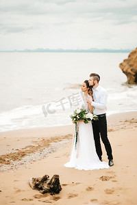 幸福的新人摄影照片_年轻的新人和新娘在沙滩上走在婚礼上