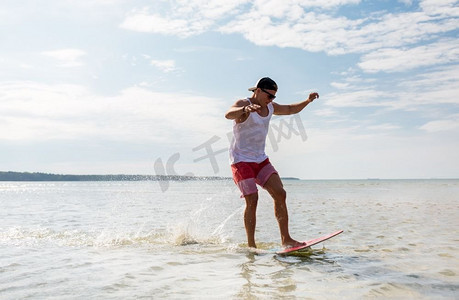 滑板、水上运动和人的概念-快乐的年轻人在夏日海滩上玩滑板。一名年轻男子在夏日海滩上玩滑板