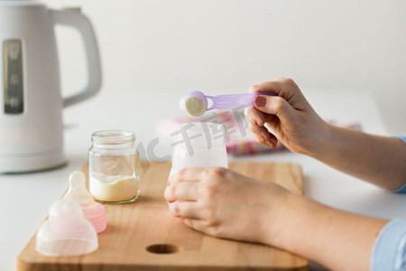 食物和营养概念-母亲手持婴儿奶瓶和勺子准备婴儿配方奶。用手用瓶子和勺子制作配方奶