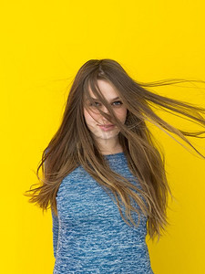 一位美丽积极的年轻女子玩耍着黄色背景下孤立的丝质长发