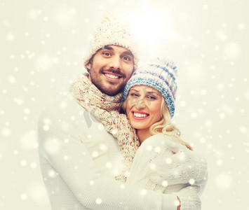 冬天，爱情，情侣，圣诞节和人的概念-戴着帽子和围巾拥抱微笑的男人和女人。一对穿着冬衣的微笑情侣拥抱着