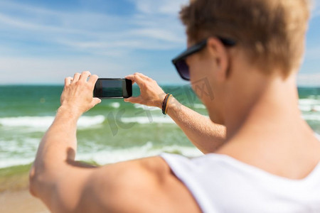 暑假和人概念-有智能手机的年轻人在海滩拍摄海。男子与智能手机拍摄在夏季海滩