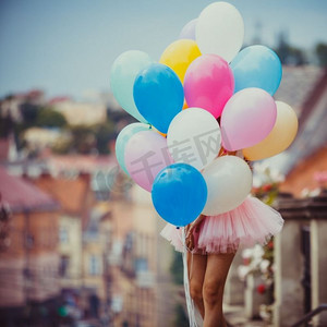 活动大气球摄影照片_一个拿着五颜六色的乳胶大气球的漂亮女孩在古镇的街道上摆姿势。带着五颜六色的乳胶气球的女孩