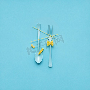 叉子和勺子的创造性静物照片与生的意大利面在蓝色背景。