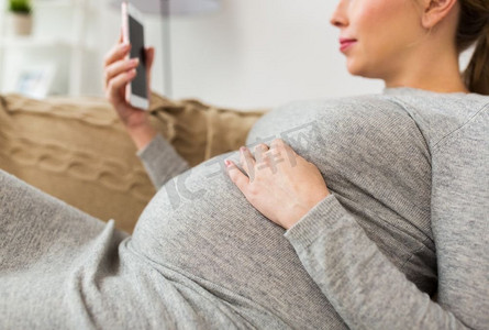怀孕、科技和人的观念--家中智能手机拍摄的快乐孕妇特写。家里有智能手机的快乐孕妇