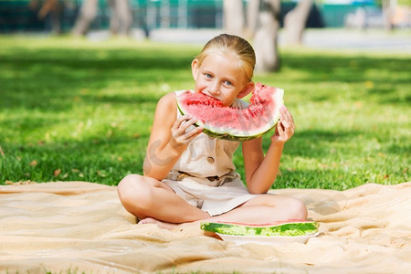 吃西瓜的女孩。公园里的可爱女孩吃着多汁的西瓜