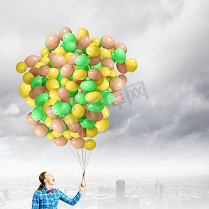 一堆彩色衣服摄影照片_拿着气球的女人。穿着休闲衣服的年轻女子手里拿着一堆彩色气球