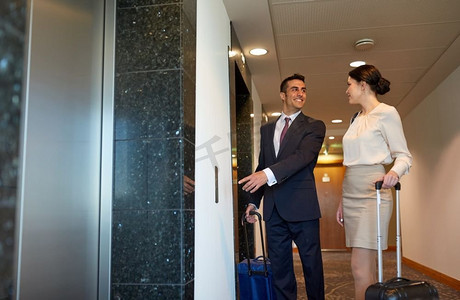 商务旅行和人的概念-男人和女人在酒店电梯里提着旅行包。商务团队带着旅行包在酒店电梯旁