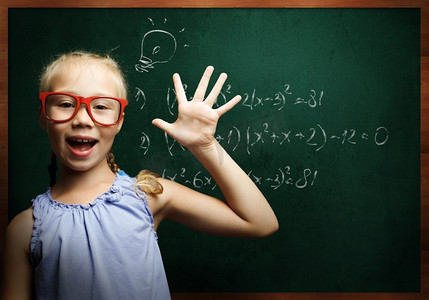 聪明的女学生。戴着红眼镜的天才女孩在黑板上写着公式