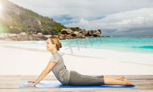 健身、运动和人的概念-在热带海滩异国情调的背景下，女人在垫子上做狗狗瑜伽姿势。一名女子在海滩上摆出狗的姿势做瑜伽