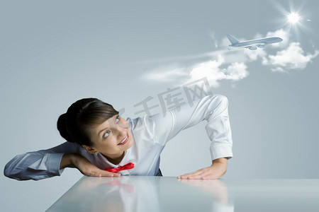 空姐。一名年轻女子俯身在桌子上方，看着天空中的飞机