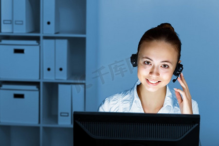 少妇在企业佩带在头戴式耳机工作与计算机