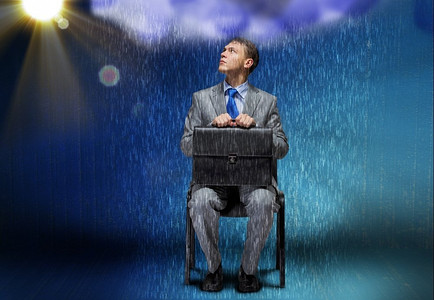雨中的人摄影照片_商业上的挑战。陷入困境的商人坐在雨中的概念形象