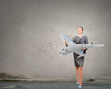 手拿车票摄影照片_飞机或商务旅行的概念。一位迷人的女商人手里拿着飞机模型