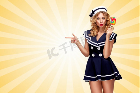 糖果卡通摄影照片_在卡通风格的背景下，一个棒棒糖指向旁边的惊艳的水手女孩。