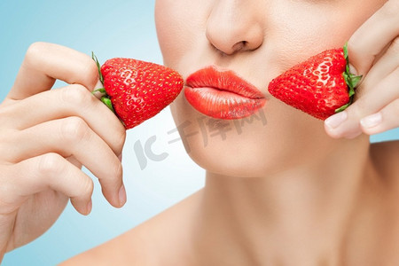 一幅富有创意的肖像，画中一个美丽的女孩渴望地将多汁的草莓放在嘴唇旁。