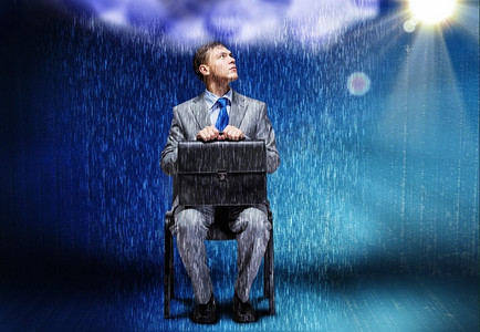 商业上的挑战。陷入困境的商人坐在雨中的概念形象