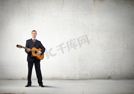 弹吉他的人。一名穿着黑色西装的年轻人弹着原声吉他