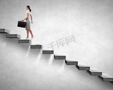 爬楼梯女摄影照片_在职业阶梯上往上爬。年轻女商人走上楼梯代表成功理念