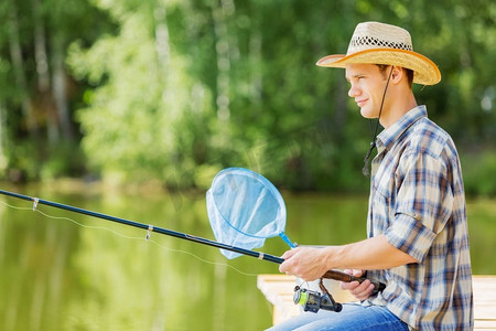 夏季钓鱼年轻人在帽子坐在桥和钓鱼