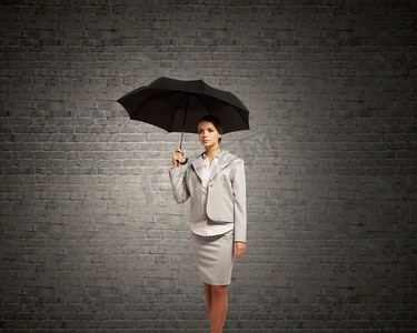 撑着伞的女人。年轻漂亮的女商人穿着西装，撑着黑色的雨伞