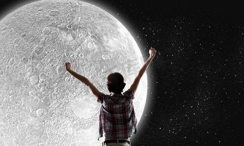 女孩仰望天空摄影照片_满月。举起双手仰望天空中月亮的年轻女子的背影