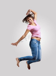 年轻女子又跳又跳。非常现代、苗条的嘻哈风格的女人在灰色的背景上跳着舞