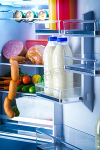 冰箱里的食物摄影照片_敞开的冰箱里装满了食物。关注冰箱里的几瓶牛奶