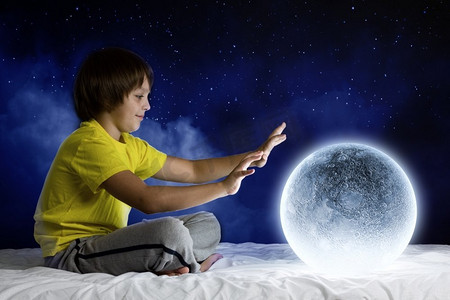可爱月球摄影照片_晚上做梦。可爱的男孩坐在床上与月球行星