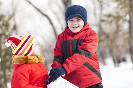 可爱的男孩和女孩在冬季公园堆雪人。冬季活动小游戏